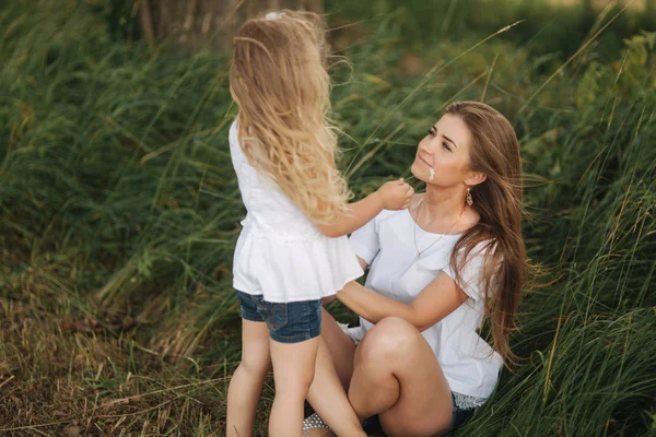 Attractive Mom and blonde hair daughter sits on road near big alley. They smile and look to natune