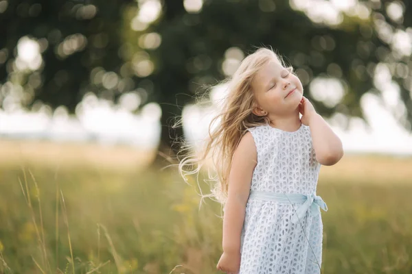 Klein meisje in hemelsblauw jurk staan in het veld voor grote boom — Stockfoto