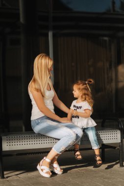 Anne ve kız açık havada şehirde. oynamak ve eğlenmek. Şehirde birlikte eğleniyor moda mutlu anne ve çocuk kızı. Onlar mall yakınındaki bankta oturuyorlar