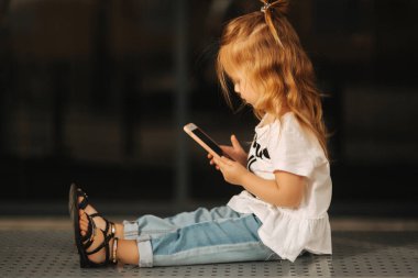 Küçük kız bankların üzerinde oturan ve telefonunuzun ve alışveriş merkezi