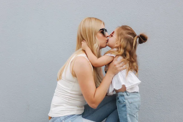 Uma bela traça com a filha. Cabelo loiro feminino. Fundo cinzento. Melhores amigos — Fotografia de Stock