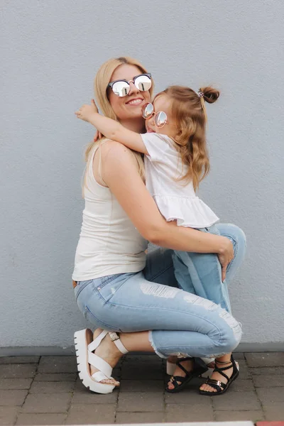 Uma bela traça com a filha. Cabelo loiro feminino. Fundo cinzento. Melhores amigos — Fotografia de Stock