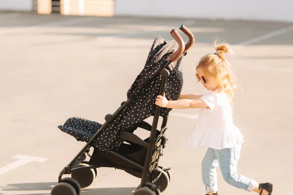 Una niña está empujando su carruaje de bebé — Foto de Stock