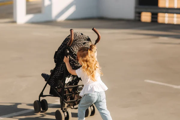 Una niña está empujando su carruaje de bebé — Foto de Stock