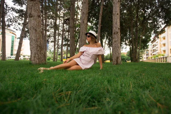 Menina bonita em vestido e chapéu no parque. Grama verde e ensolarado. Contexto das árvores — Fotografia de Stock