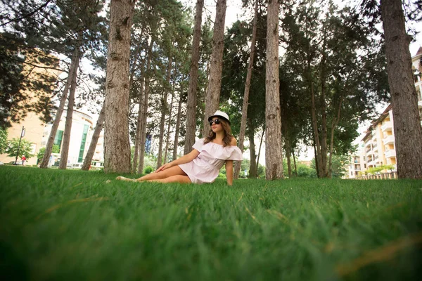 Menina bonita em vestido e chapéu no parque. Grama verde e ensolarado. Contexto das árvores — Fotografia de Stock