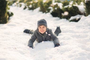 Kış giysileri içinde bir oğlan kar atlar. Mutlu tatil
