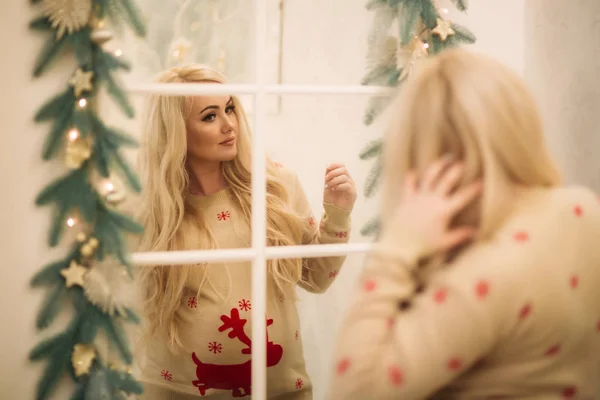 En ganska gravid blond hår kvinna i jul tröja står nära spegeln. Vintern anda. Gott Nytt År — Stockfoto
