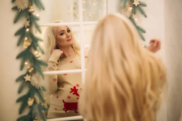 En ganska gravid blond hår kvinna i jul tröja står nära spegeln. Vintern anda. Gott Nytt År — Stockfoto