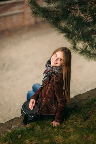 Attenta ragazza siede vicino all'argine. Capelli biondi e giacca marrone. Primavera — Foto Stock