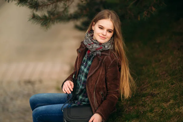 Aantrekkelijke jonge meisje door de dijk zit. Blond haar en bruine jas. Lente — Stockfoto