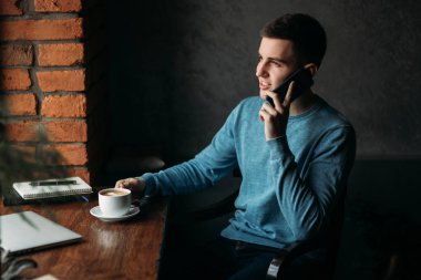 Yakışıklı çocuk kafede kahve içme. Pencerenin laptop ve defter ile oturuyor