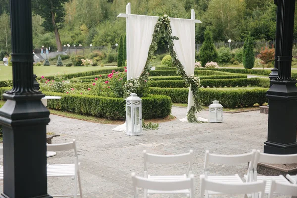 Свадебные украшения на открытом воздухе. Цветочный декор красивой белой арки. Вид на деревья — стоковое фото