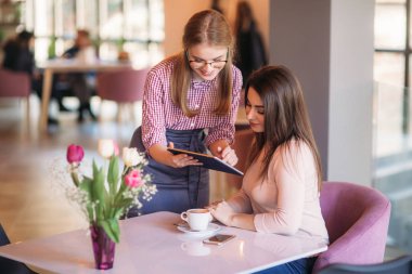 Kahve dükkanındaki müşteriden sipariş almak için tablet bilgisayar kullanan çekici genç bir garson.
