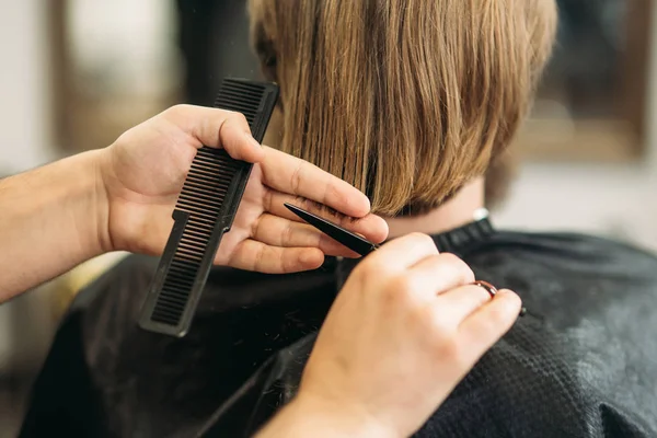 Master cuts hair and beard of men in the barbershop, hairdresser makes hairstyle for a young man