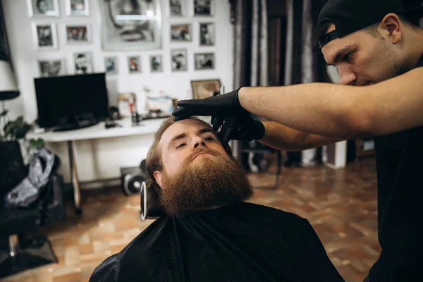 Bearded man with long beard getting stylish hair shaving , haircut , with razor by barber in barbershop
