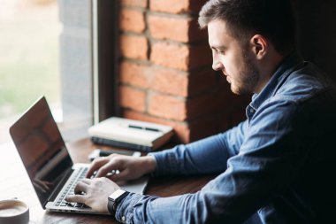 Bir sakallı bir dizüstü bilgisayar bir kafede kullanır.