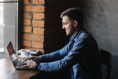 Bir sakallı bir dizüstü bilgisayar bir kafede kullanır.