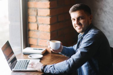 Bir sakallı bir dizüstü bilgisayar bir kafe ve içecek kahve kullanır.