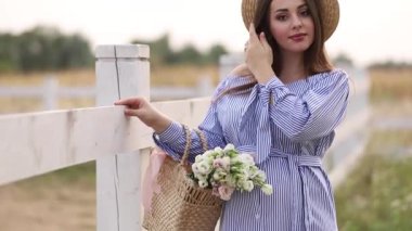 Mavi elbise yürüyüş güzel hamile kadın çiftlik duydum. Buket çiçek ile örme çanta. Arka plan ağaç ve dağlar. Ağır çekim