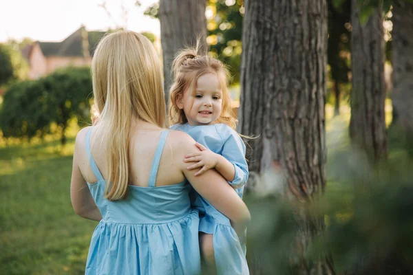 Junge schöne Frau mit ihrer kleinen süßen Tochter. Kleine Tochter umarmt Mutter im Sommerpark — Stockfoto