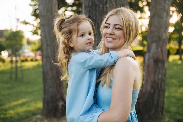 Young beautiful woman with her little cute daughter. Young daughter hugs mother in summer park — Stock Photo, Image