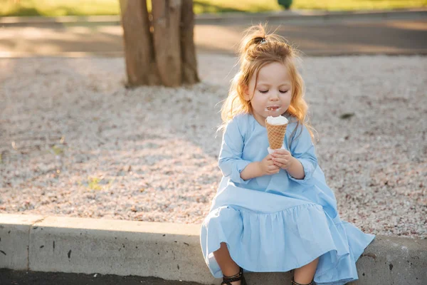 Красивая маленькая девочка в синем платье ест мороженое — стоковое фото