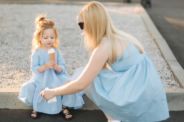 Fetiță frumoasă într-o rochie albastră mâncând o înghețată, mama ajută și șterge gura — Fotografie, imagine de stoc