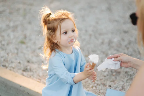 Красивая маленькая девочка в синем платье ест мороженое — стоковое фото