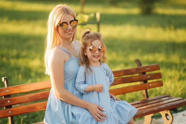 Moeder en zijn dochtertje zitten op een bankje in het park — Stockfoto