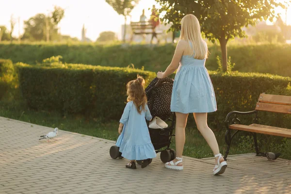 Kleine Tochter hilft Mama, den Kinderwagen zu schieben. glückliche Familie — Stockfoto