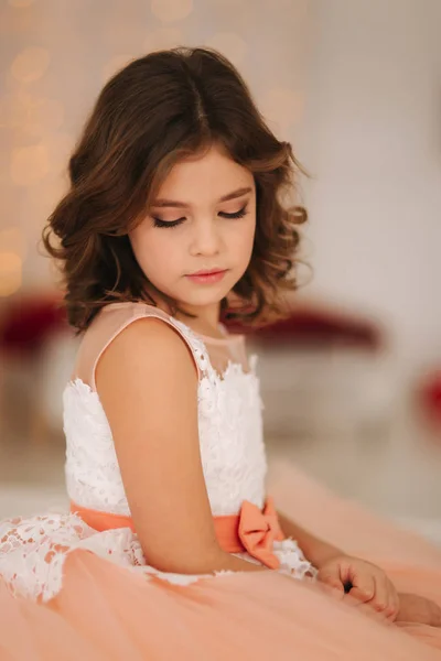 Kleines schönes Mädchen mit braunen Haaren in einem pfirsichfarbenen Kleid. posiert für einen Fotografen — Stockfoto