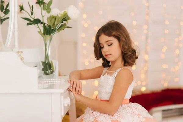 Kis lány ül a fehér zongora által. Fehér virágok, a zongorán. A gyönyörű ruha lány modell — Stock Fotó