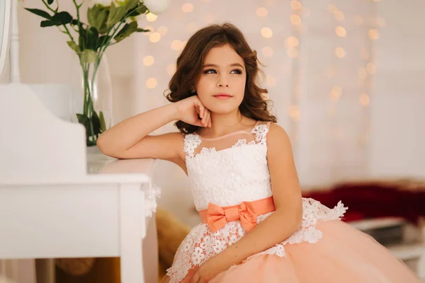 Meisje zit door de witte piano. Witte bloemen op de piano. Meisje model in mooie jurk — Stockfoto