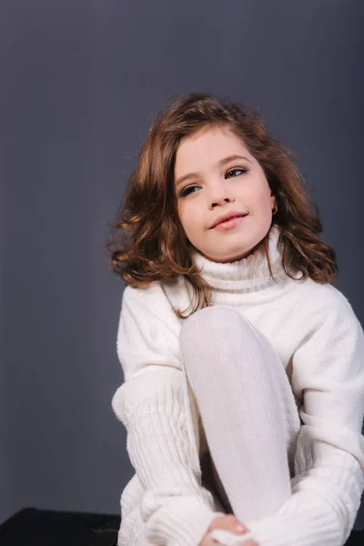 Kleines schönes Mädchen mit braunen Haaren in weißem Pullover. Studio. eine Prinzessin posiert für einen Fotografen. Make-up und Frisur — Stockfoto