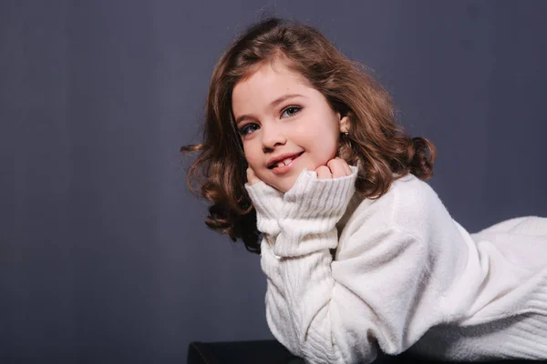 Niña hermosa con el pelo castaño en un suéter blanco. Estudio. Una princesa posa para un fotógrafo. Maquillaje y peinado —  Fotos de Stock