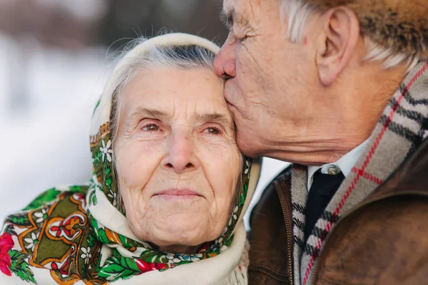 老夫妇的肖像。老人亲吻他的妻子在重量。冬天的时候, 老夫妇在公园里散步。幸福的家庭。黄金婚礼 — 图库照片