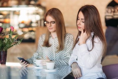 Kapuçino içiyor ve smartphone kullanarak bir kafede oturan iki kız. Modern kız