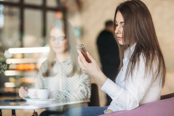 Twee meisjes zitten in een cafe cappuccino drinken en het gebruik van de smartphone. Moderne meisje — Stockfoto