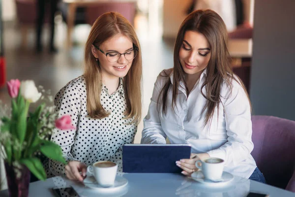 Zwei Mädchen benutzen ein Tablet, während sie in einem Café sitzen und Kaffee trinken. Geschäftsfrau — Stockfoto