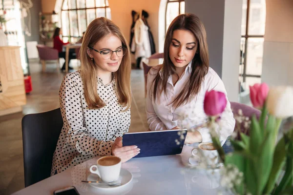 Zwei Mädchen benutzen ein Tablet, während sie in einem Café sitzen und Kaffee trinken. Geschäftsfrau — Stockfoto