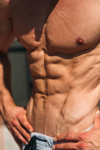 Un joven atleta entrena en el gimnasio. Muestra los músculos adbominales. Afuera. — Foto de Stock