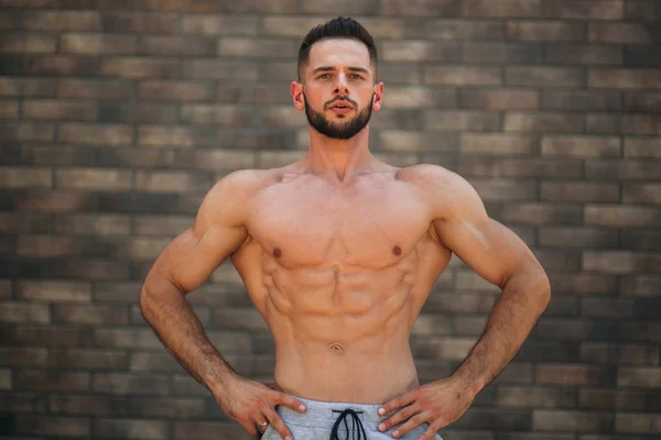 Jeune athlète posant avec un torse pour la photographie sur un fond de mur de briques. Bodybuilder, athlète avec muscles pompés, sauvetage des seins et des bras — Photo