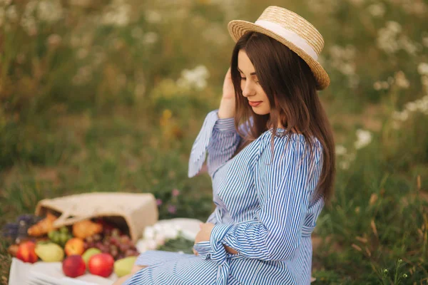 Mujer embarazada joven sentada en el campo y relajarse. Se llevó una cesta de frutas. Verano — Foto de Stock