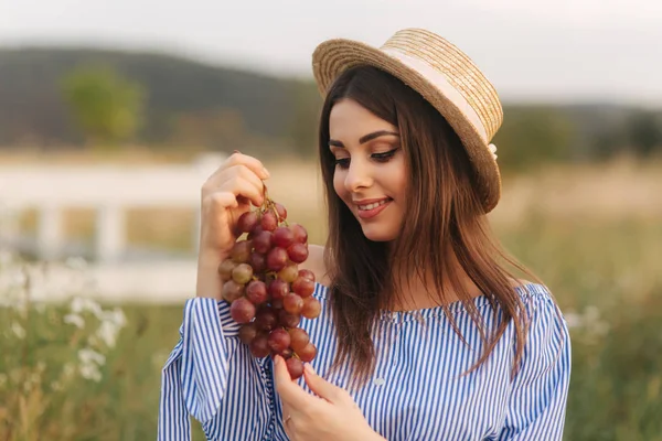 Hermosa mujer embarazada mostrar y comer uvas rojas. Comida saludable. Frutas frescas. Mujer feliz sonrisa — Foto de Stock