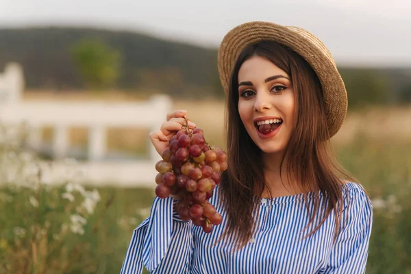 Hermosa mujer embarazada mostrar y comer uvas rojas. Comida saludable. Frutas frescas. Mujer feliz sonrisa — Foto de Stock