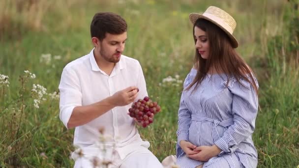 Hermosa pareja hombre y mujer embarazada comen uvas rojas. Comida saludable. Frutas frescas. Mujer feliz sonrisa — Vídeo de stock