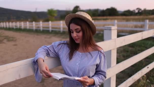 Bella donna incinta ha letto il libro in fattoria. Sta vicino al recinto e guarda dentro al libro. Rilassati — Video Stock