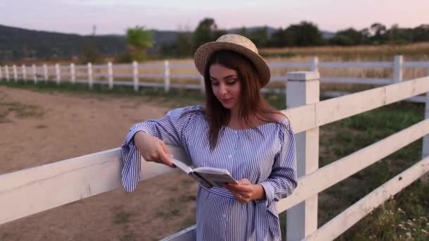 Beautiful pregnant woman read the book on the farm. She stand by the fance and look in to the book. Relax — Stock Video