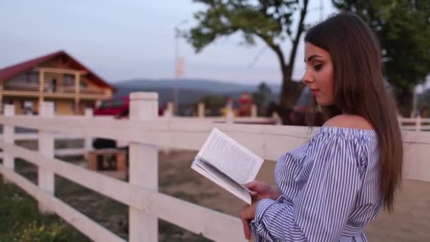 Красивая беременная женщина прочитала книгу на ферме. Она стоит у мотылька и смотрит в книгу. Расслабьтесь — стоковое видео